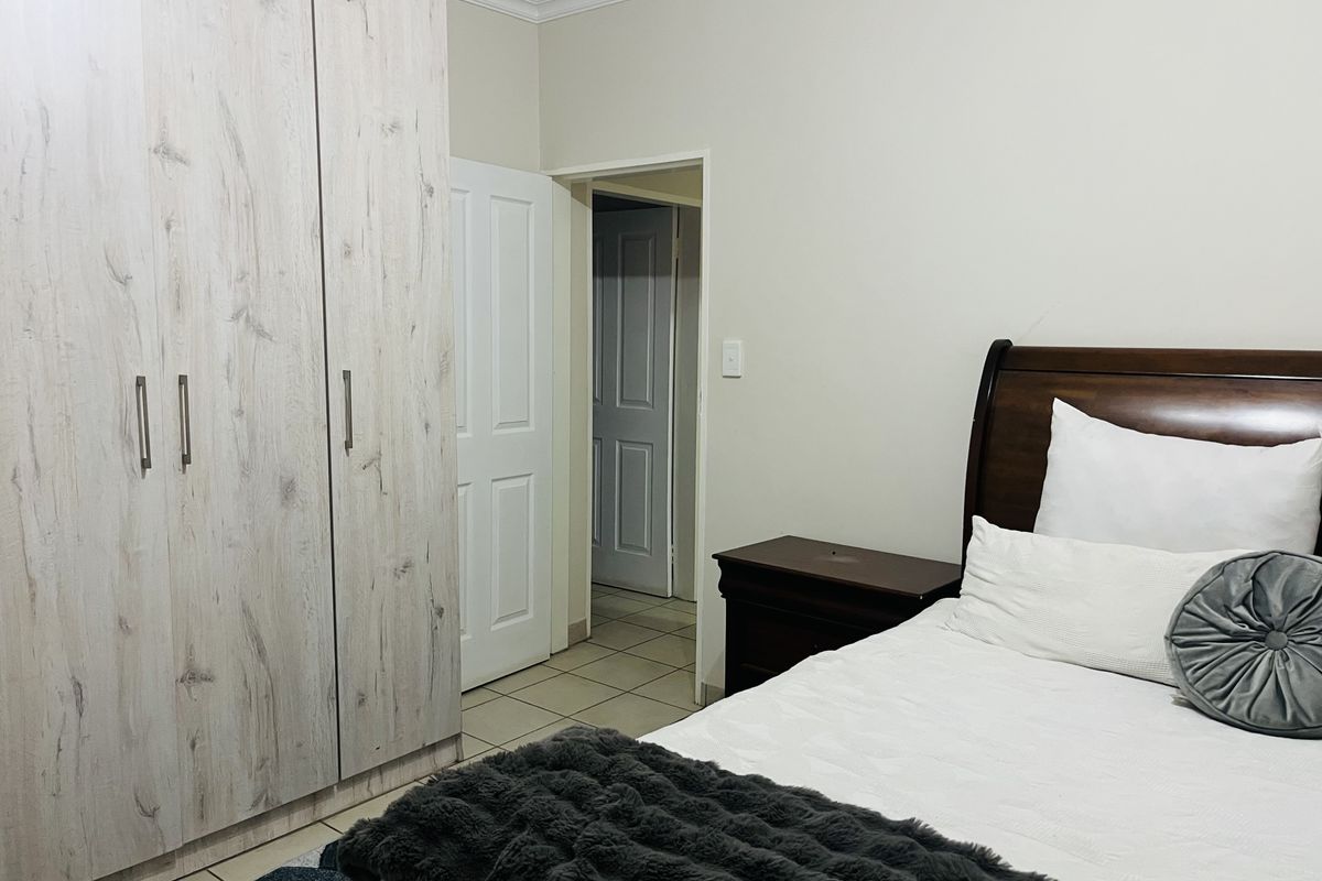 A well-maintained bedroom featuring light wood-grain built-in cupboards, neutral wall finishes, and tiled flooring, providing a clean and functional living space.