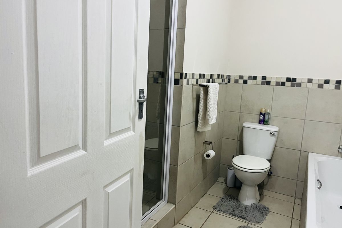 A functional bathroom featuring a bathtub, a separate shower enclosure, and neutral wall and floor tiling with a decorative mosaic border.