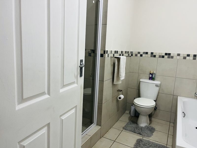 A functional bathroom featuring a bathtub, a separate shower enclosure, and neutral wall and floor tiling with a decorative mosaic border.