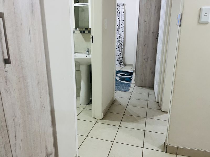 A tiled hallway providing access to a bathroom with a pedestal basin and featuring built-in storage cupboards.