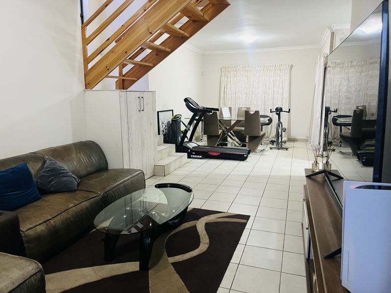 Open-plan living area featuring tiled flooring and a wooden staircase, providing a versatile space for relaxation and dining.