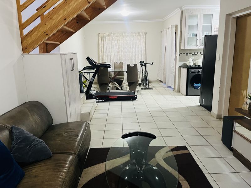 Open-plan living and kitchen area featuring tiled flooring and a wooden staircase, offering a functional layout for daily living.