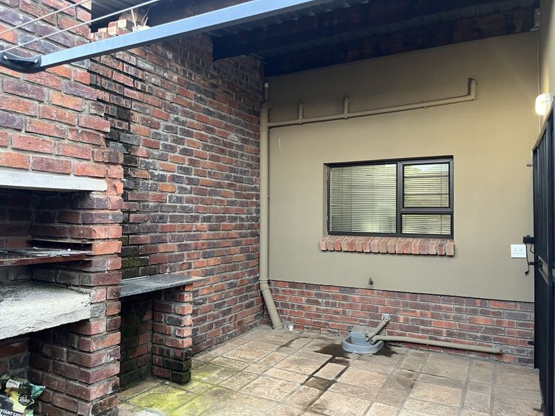 Covered patio area featuring a built-in brick braai, tiled flooring, and exposed brick wall finishes, suitable for outdoor entertaining.