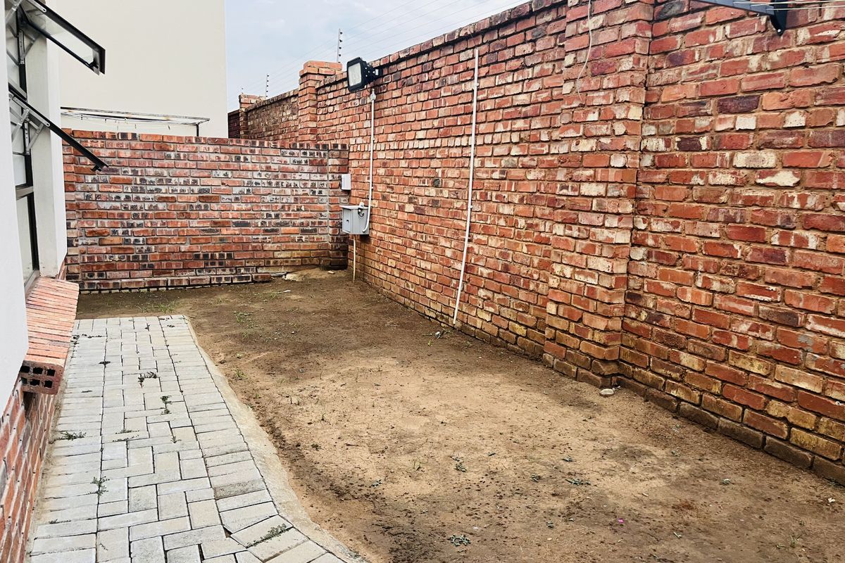 A private rear courtyard featuring a paved walkway, high brick boundary walls, and an open soil area ready for landscaping or garden development.