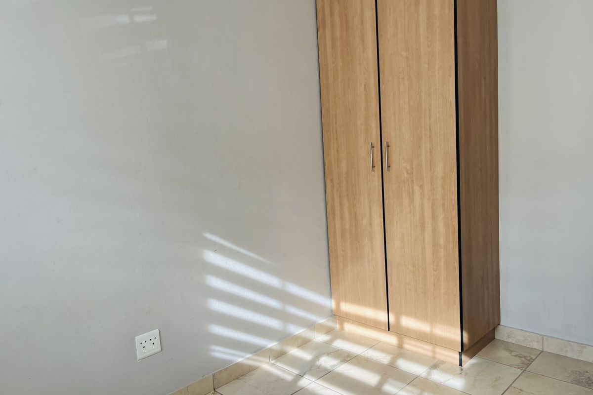 A bedroom featuring a built-in wooden wardrobe and tiled flooring, illuminated by natural light.