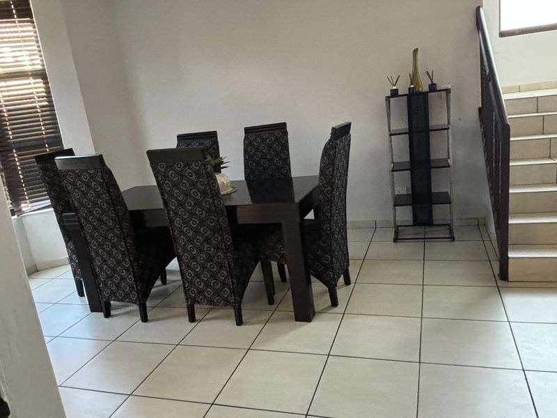 A dining area featuring tiled flooring, a staircase with a metal railing, and large windows with fitted blinds.