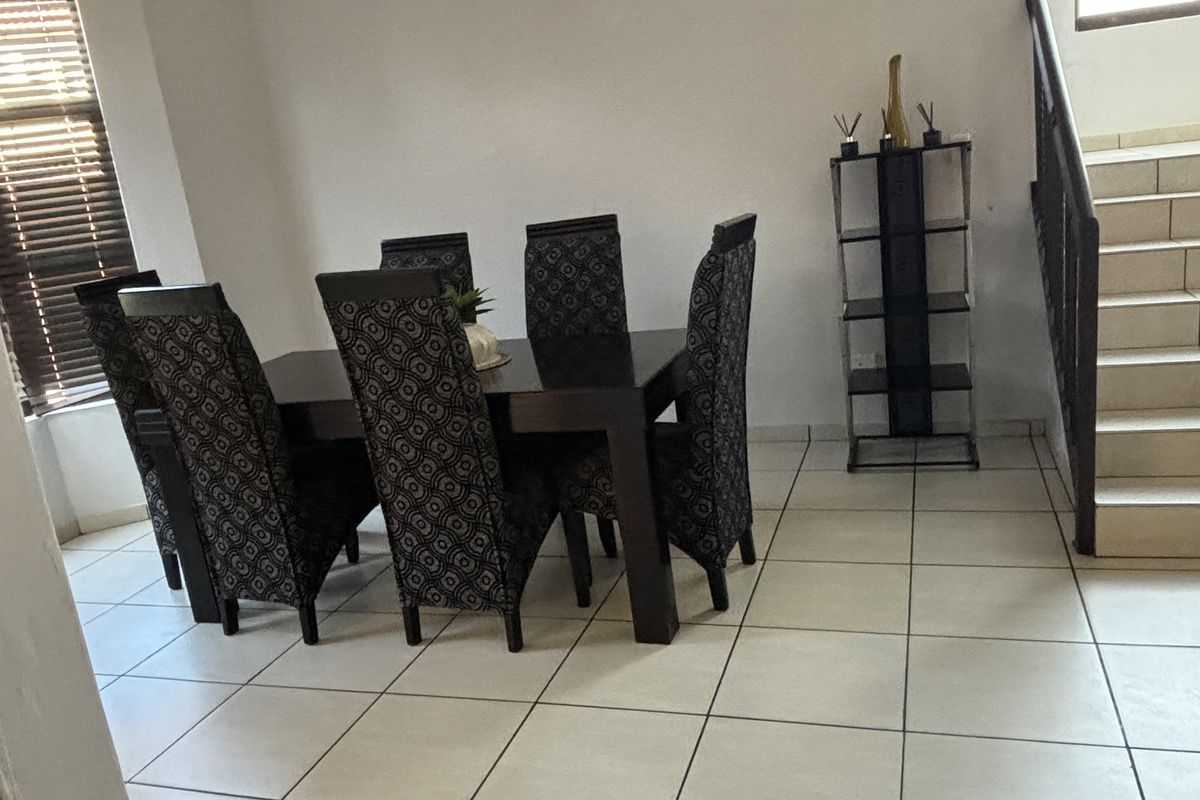 A dining area featuring tiled flooring, a staircase with a metal railing, and large windows with fitted blinds.