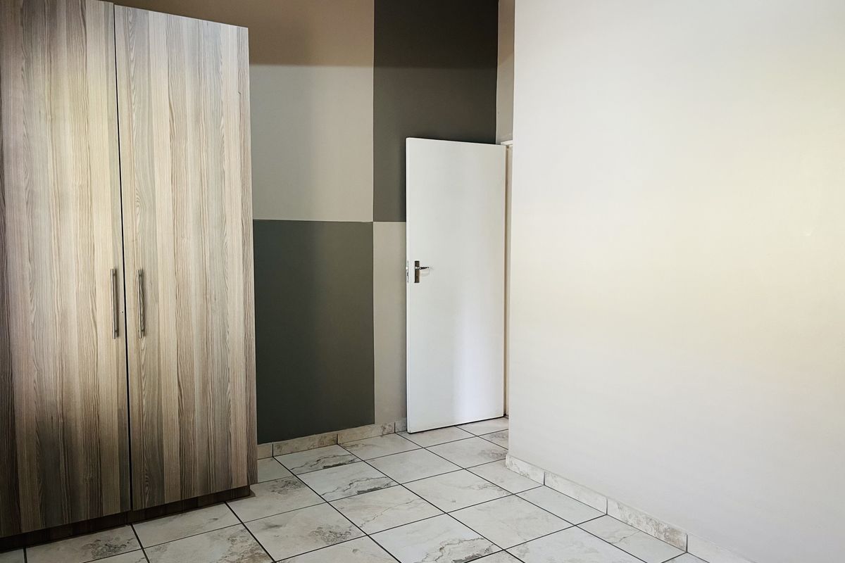 A bedroom featuring tiled flooring, a built-in wooden wardrobe, and a decorative painted feature wall.