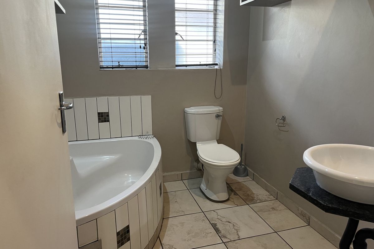 A functional bathroom featuring a corner bathtub with tiled surround, a pedestal-style basin, and a standard toilet with tiled flooring.