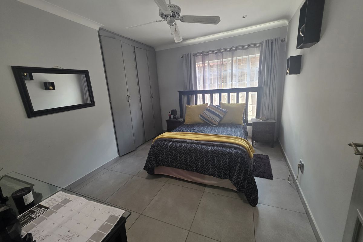 A well-maintained bedroom featuring neutral floor tiles, built-in cupboards, and a ceiling fan, offering a clean and functional living space.