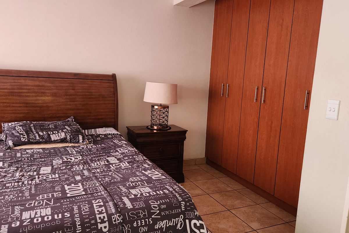 A bedroom featuring tiled flooring and a large built-in wooden wardrobe providing ample storage space.