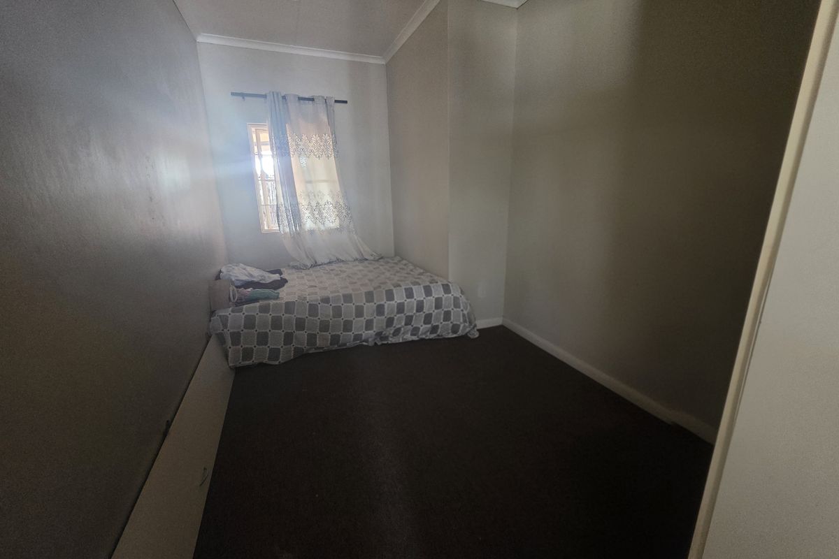 A compact bedroom featuring dark carpeting, neutral wall tones, and a single window providing natural light.