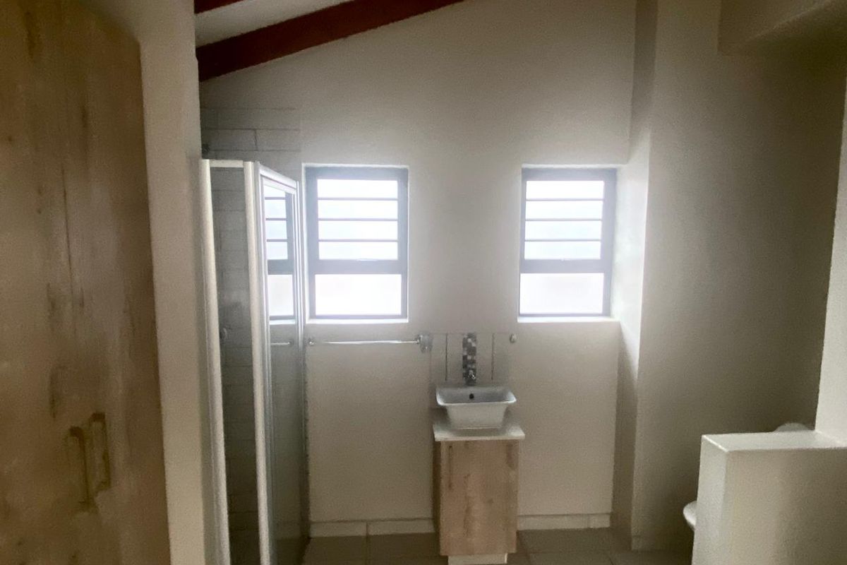 A functional bathroom featuring a shower enclosure, a modern vessel sink vanity, and exposed timber roof beams under a vaulted ceiling.