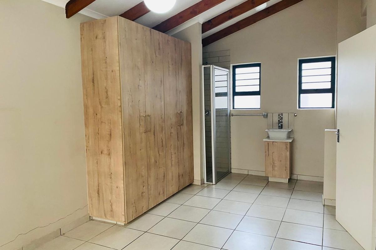 A bedroom featuring exposed timber ceiling beams, built-in wooden cabinetry, and an en-suite shower area with a vanity basin.