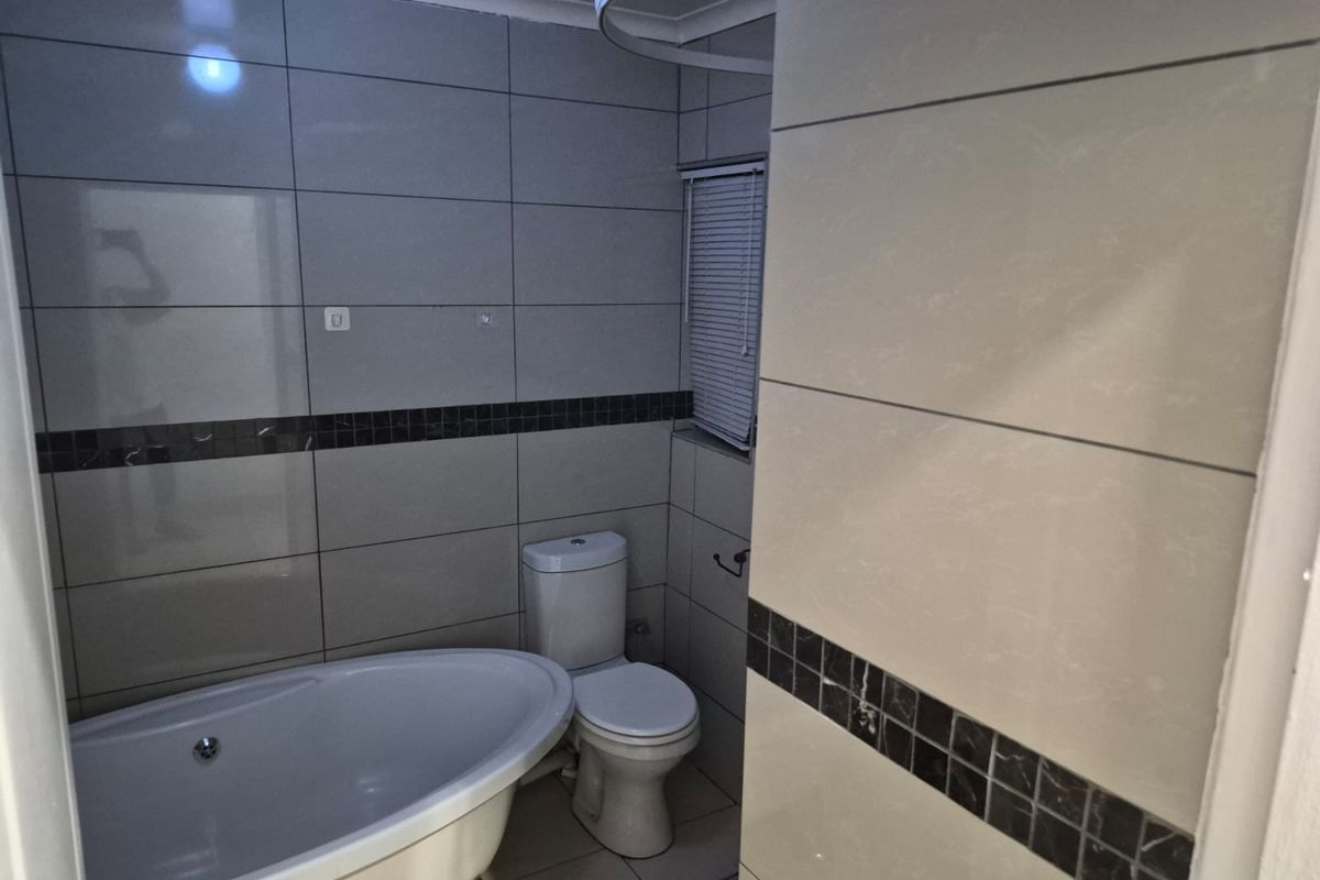 A functional bathroom featuring a freestanding bathtub, a standard toilet, and tiled walls with decorative mosaic accents.