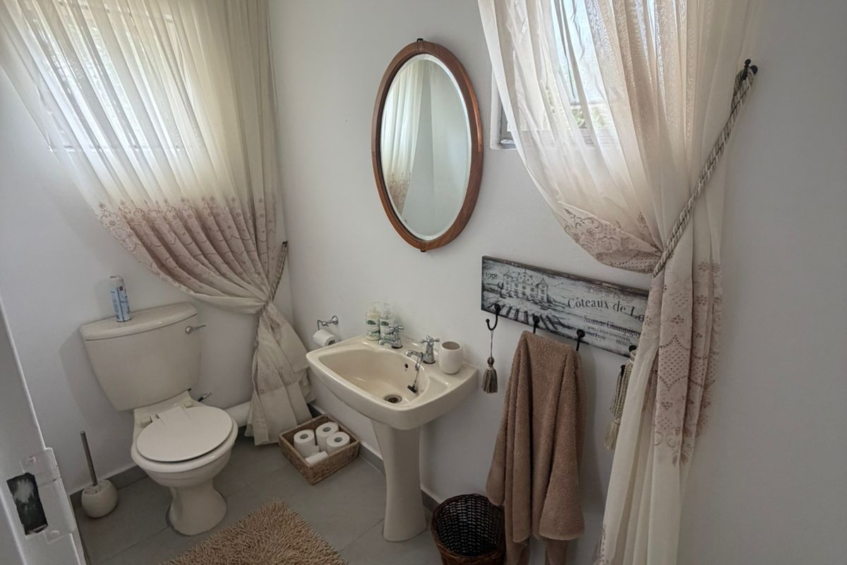 A functional guest bathroom featuring a pedestal basin, toilet, and tiled flooring, finished with neutral tones and natural light.