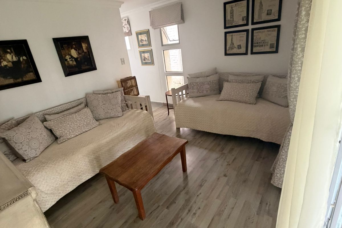 A cozy living room featuring light wood-look flooring, neutral walls, and large windows that provide natural light.