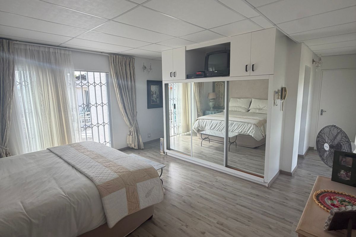 A bedroom featuring built-in mirrored wardrobes, light wood-look flooring, and sliding glass doors leading to an outdoor area.