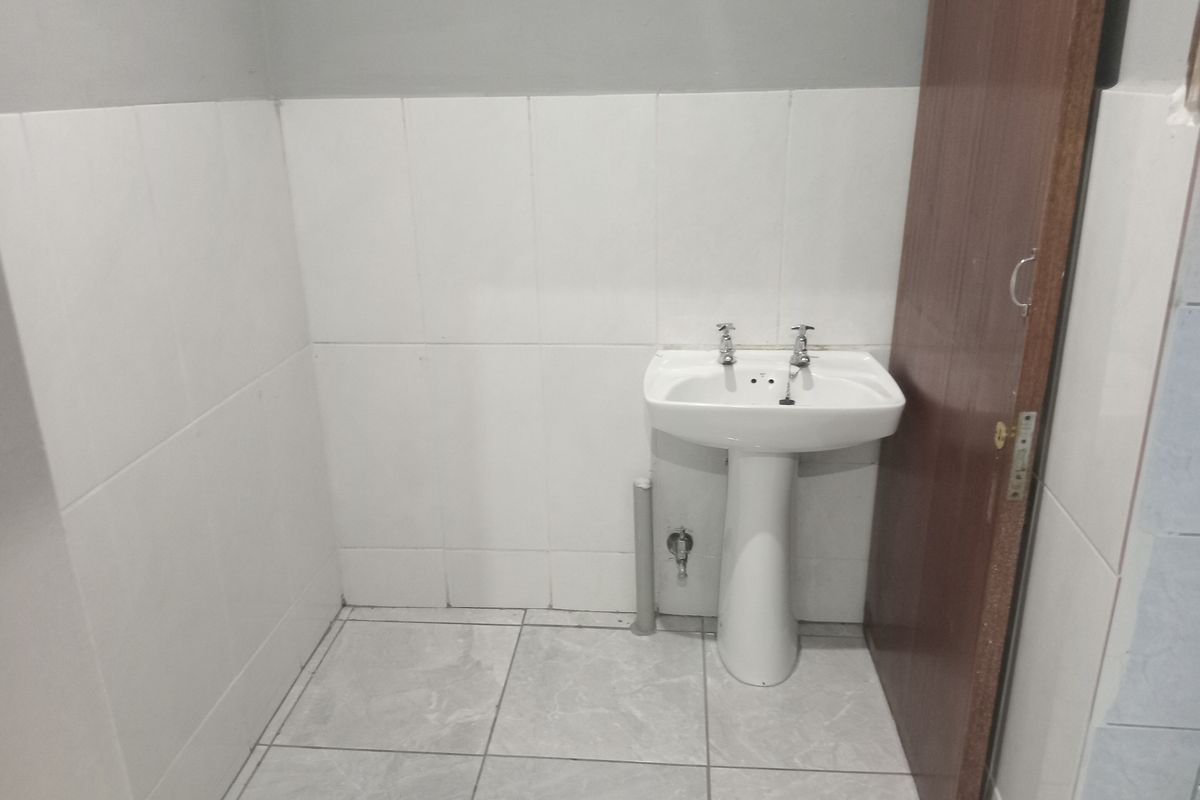 A simple, functional bathroom space featuring a white pedestal basin, tiled walls, and tiled flooring.