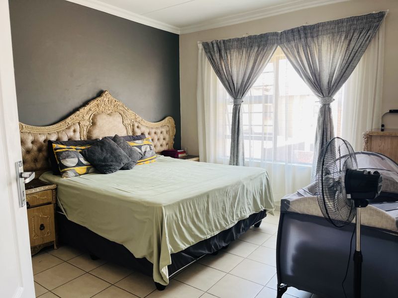 A bedroom featuring tiled flooring, a dark accent wall, and a large window with curtain treatments.