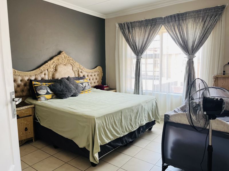 A bedroom featuring tiled flooring, a dark accent wall, and large windows with curtains, providing a functional and comfortable living space.