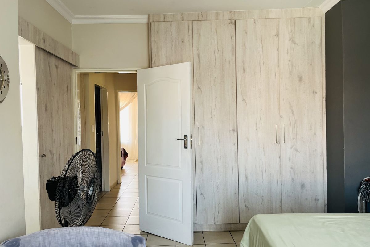 Bedroom featuring light wood-grain built-in cupboards, tiled flooring, and crown molding, with an open doorway leading to an adjacent hallway.
