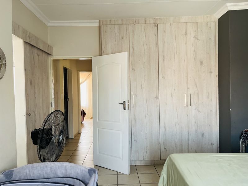 Bedroom featuring light wood-grain built-in cupboards, tiled flooring, and crown molding, with an open doorway leading to an adjacent hallway.