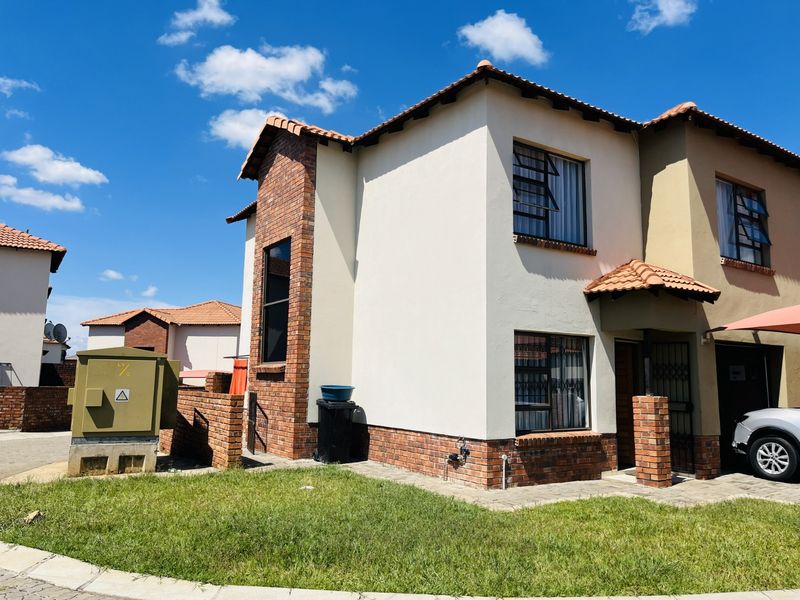 A two-story townhouse featuring a brick and plaster facade, tiled roof, and secure window bars, situated in a residential complex.