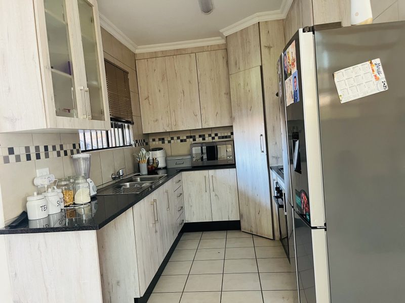 A functional kitchen featuring light wood-grain cabinetry, black granite countertops, tiled flooring, and a tiled backsplash with a decorative border.