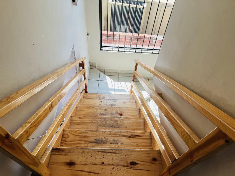 A staircase featuring wooden treads and railings, leading down to a tiled landing with a security-barred window.