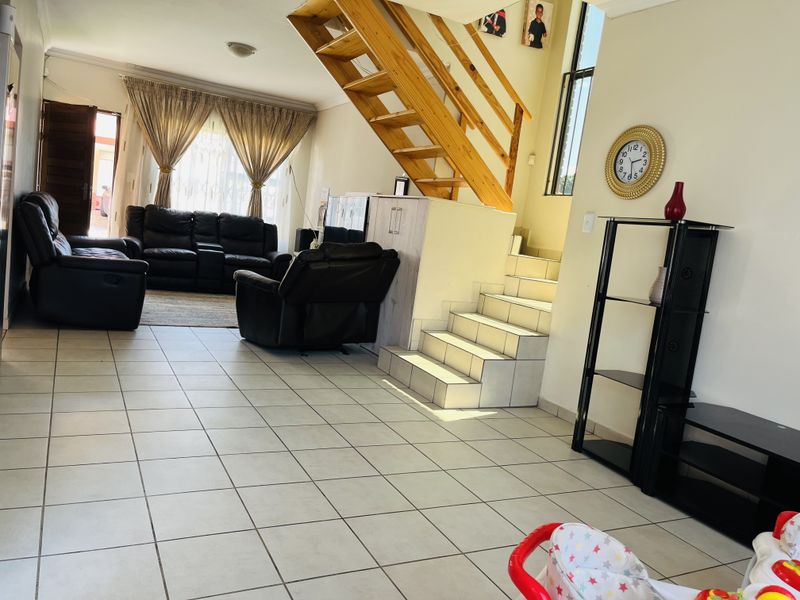 Open-plan living area featuring tiled flooring and a wooden staircase leading to the upper level, providing a functional and connected layout.