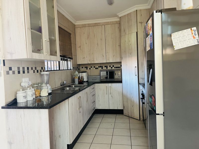 A functional kitchen featuring light wood-grain cabinetry, dark granite countertops, tiled backsplash, and ceramic floor tiles.