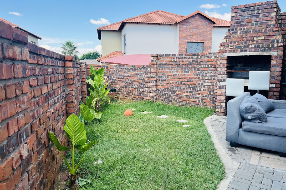 A private rear garden featuring a built-in brick braai area, paved patio section, and perimeter brick walling.