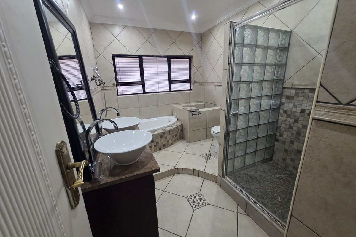 Spacious bathroom featuring a double vanity with vessel sinks, a built-in bathtub, and a separate shower enclosure with glass block detailing.
