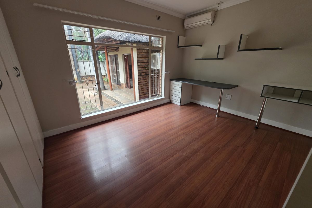 A bright bedroom featuring laminate flooring, a built-in desk with shelving, and a split-system air conditioner, with views of the rear patio.