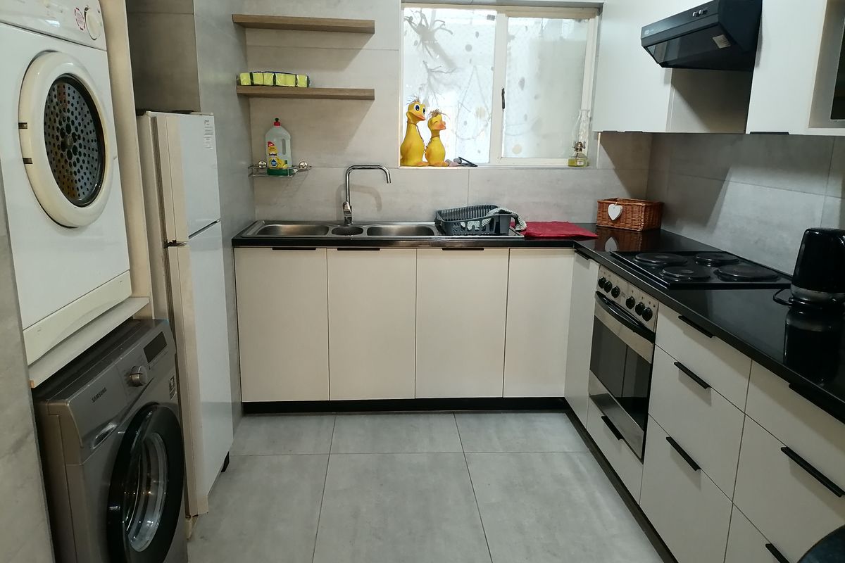 A compact, modern kitchen featuring white cabinetry, black countertops, a built-in oven, hob, extractor fan, and integrated laundry appliances.