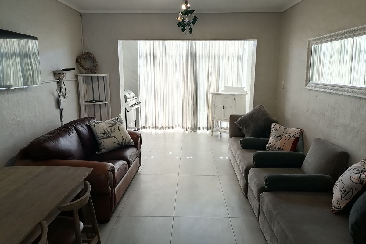 A spacious living area featuring large format floor tiles and a seamless transition to a bright, curtained patio space.