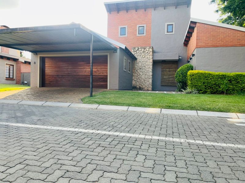 Front elevation of a modern townhouse featuring a double garage, attached carport, stone-clad accents, and a well-maintained paved driveway.