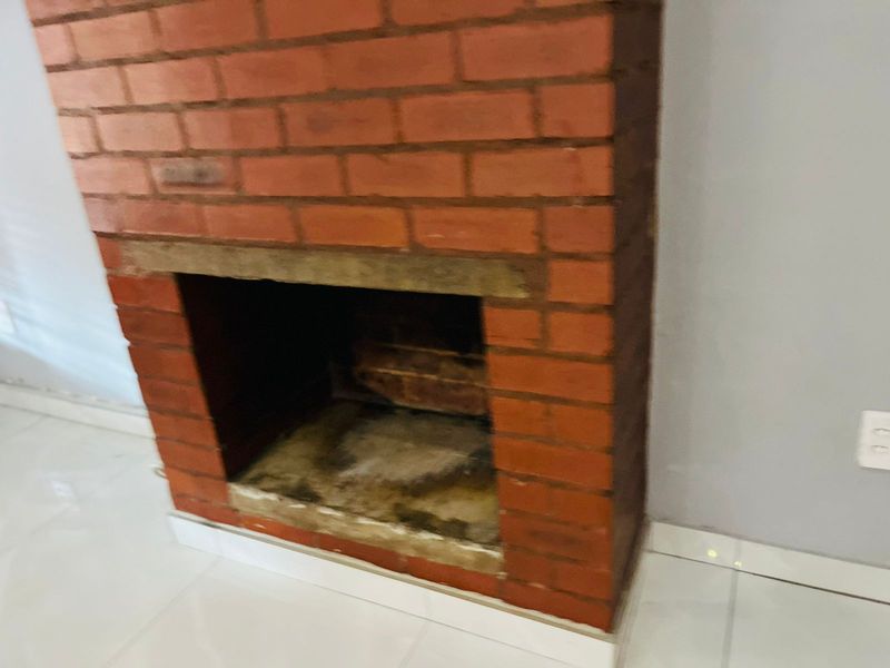 A living room area featuring a traditional exposed brick fireplace with a tiled floor, presenting a blank canvas for interior design.