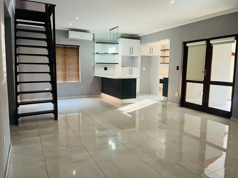 Spacious open-plan living area featuring polished tile floors, a modern kitchen island, built-in cabinetry, and a staircase leading to the upper level.