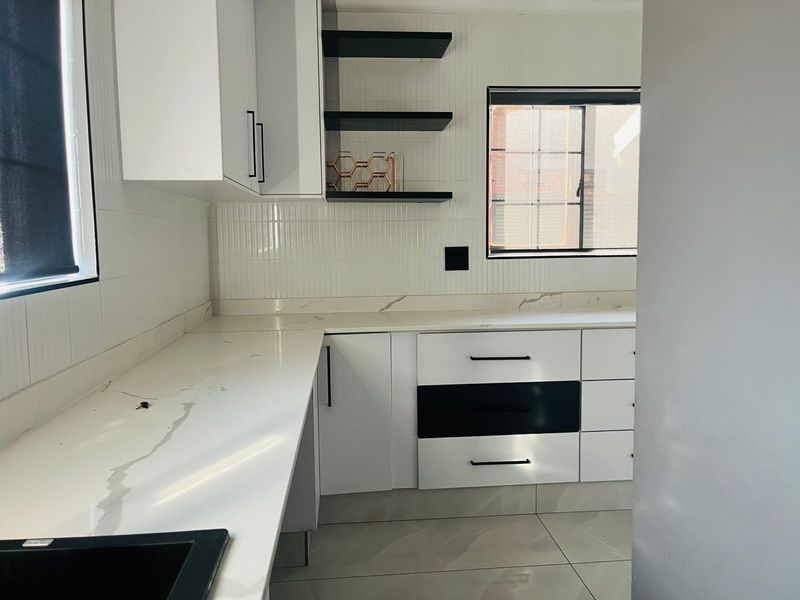 Modern kitchen featuring white quartz countertops, sleek cabinetry with black hardware, tiled backsplash, and floating shelves in a bright, clean space.