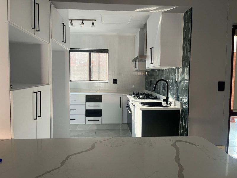 Modern kitchen featuring white cabinetry, contrasting black hardware, quartz countertops, a gas hob, and a stylish subway tile backsplash.