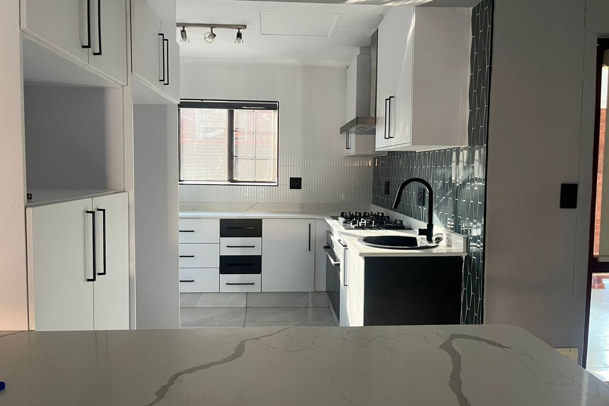 Modern kitchen featuring white cabinetry, contrasting black hardware, quartz countertops, a gas hob, and a stylish subway tile backsplash.