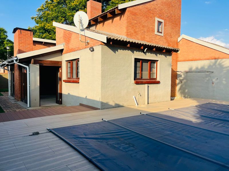 Rear exterior view of a townhouse featuring a swimming pool with a cover, timber-framed windows, and a spacious deck area.
