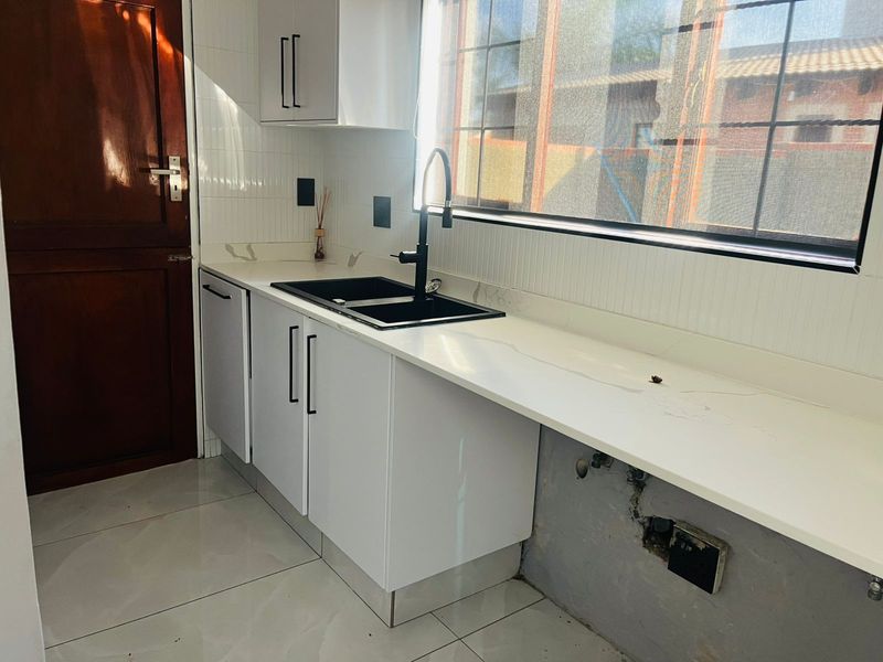 A modern kitchen area featuring white cabinetry, stone countertops, and a black sink, currently awaiting final finishing touches to the lower wall section.
