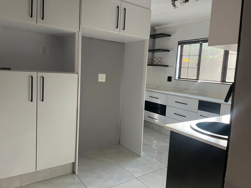 Modern kitchen featuring white and black cabinetry, stone countertops, tiled flooring, and floating shelves, offering a clean and functional workspace.