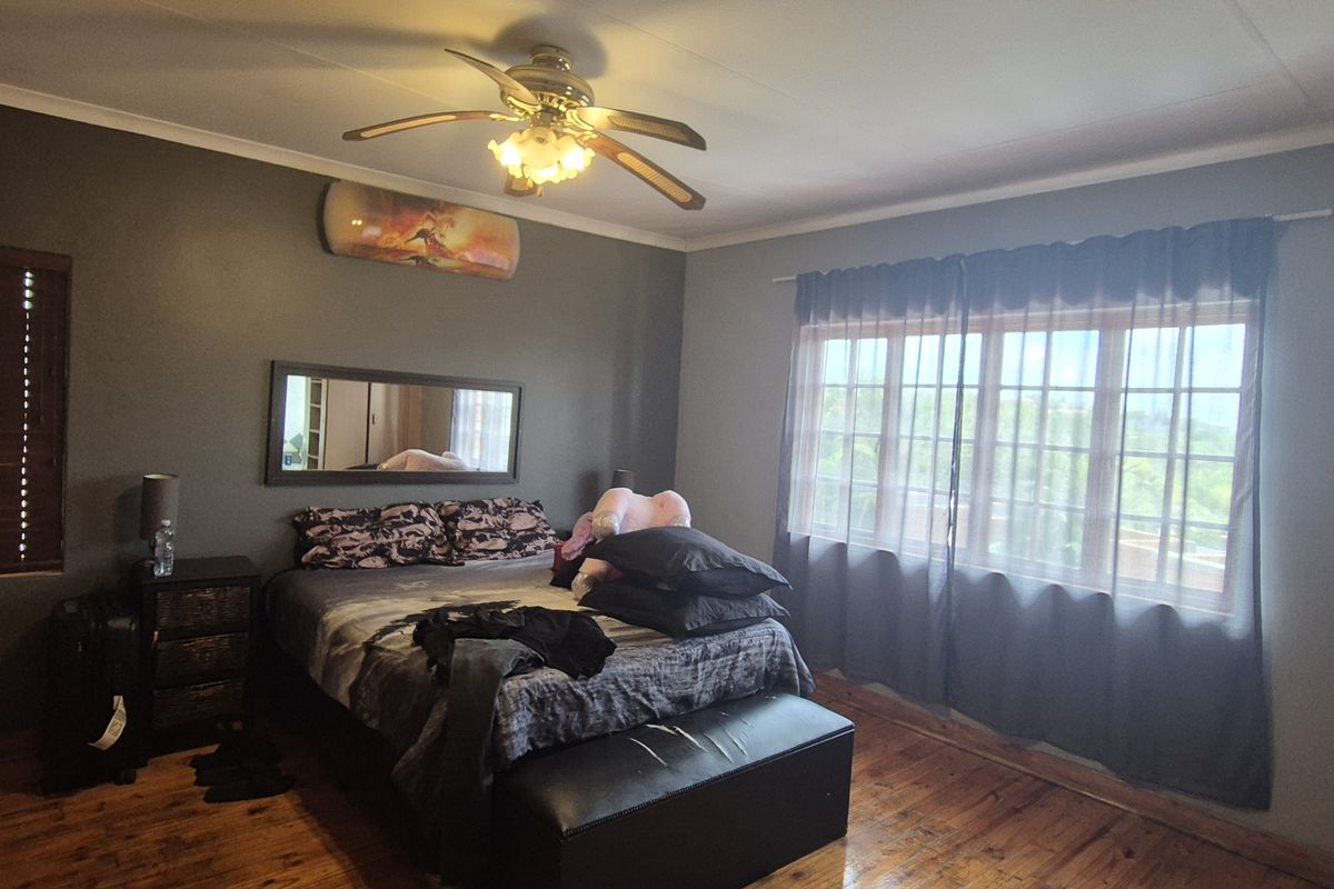 A bedroom featuring polished timber flooring, built-in cupboards, a ceiling fan, and large windows allowing for natural light.