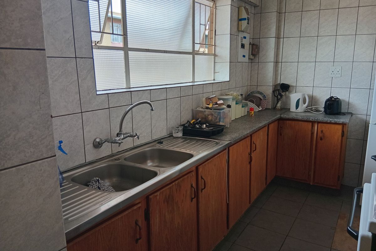 A functional kitchen featuring wooden cabinetry, double bowl stainless steel sink, laminate countertops, and tiled wall finishes.