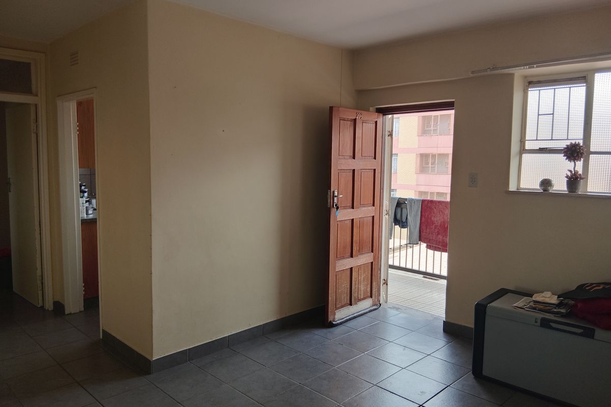 An empty living area featuring tiled flooring and direct access to a small balcony through a timber door.