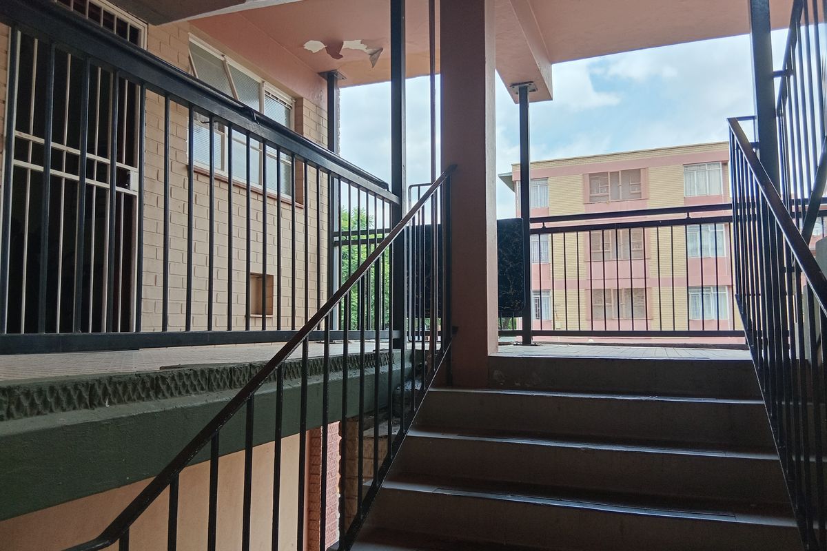Exterior view of a concrete staircase and metal balustrade leading to an apartment entrance, showing some wear to the ceiling finish.